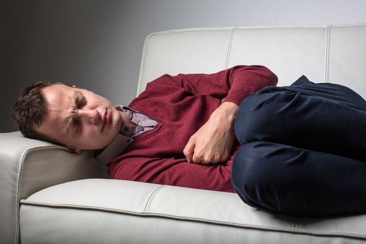 Muž trpiaci Crohnovu chorobu leží v bolestiach na gauči