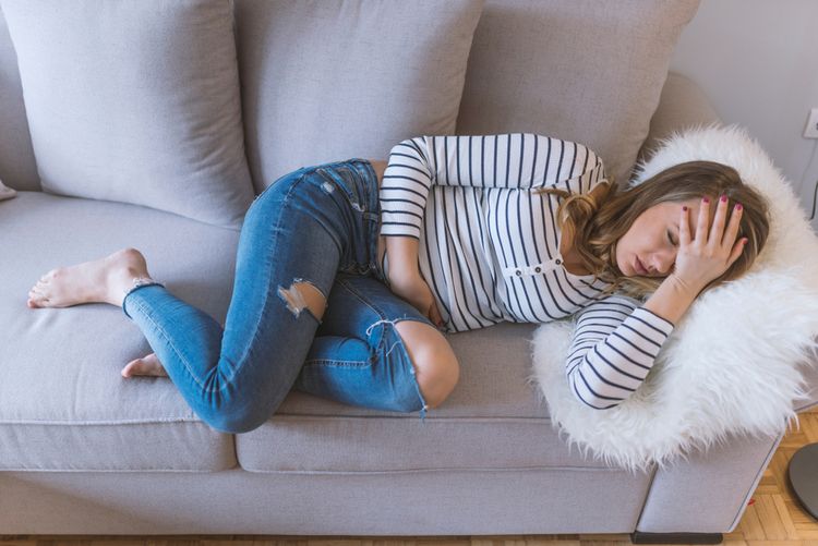 Žena s menštruačnými bolesťami ležiaca na gauči