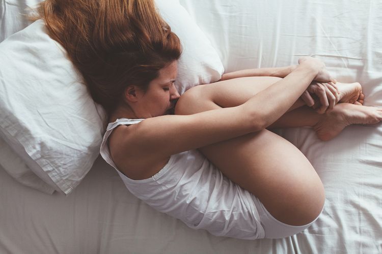 Žena s PMS - ležiaca v klbku na posteli