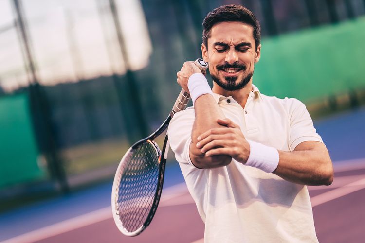 Muž s bolesťou lakťa počas hrania tenisu